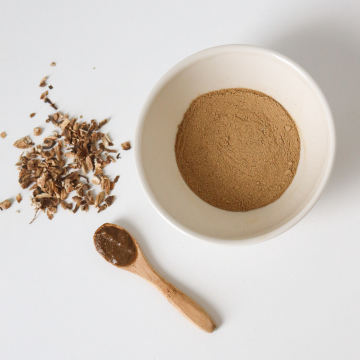 Bol blanc contenant de la poudre de kapoor kachli marron, cuillère en bois et racines séchées sur fond blanc – ingrédient ayurvédique naturel pour masque cheveux volume brillance, stimulation de la pousse, idéale pour les masque capillaire detox pour le cuir chevelu