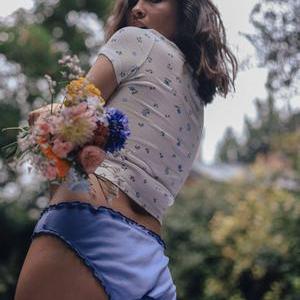 Culotte bleu pastel pour femme portée en extérieur, lingerie douce et éco-responsable, style naturel avec bouquet de fleurs.
