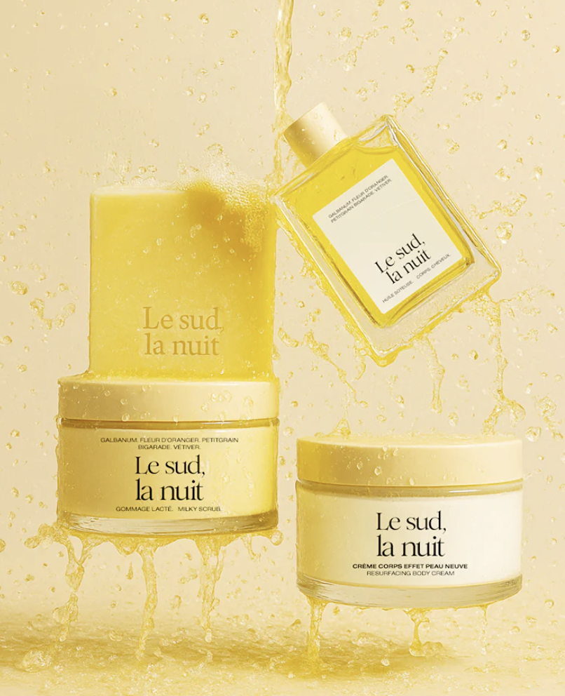 Cosmétiques de la marque refile naturals: Flacons pots en verre crèmes corps en bas de l'image et savon/flacon en verre d'huile au milieu. Liquide jaune qui éclabousse tous les produits venant d'en haut